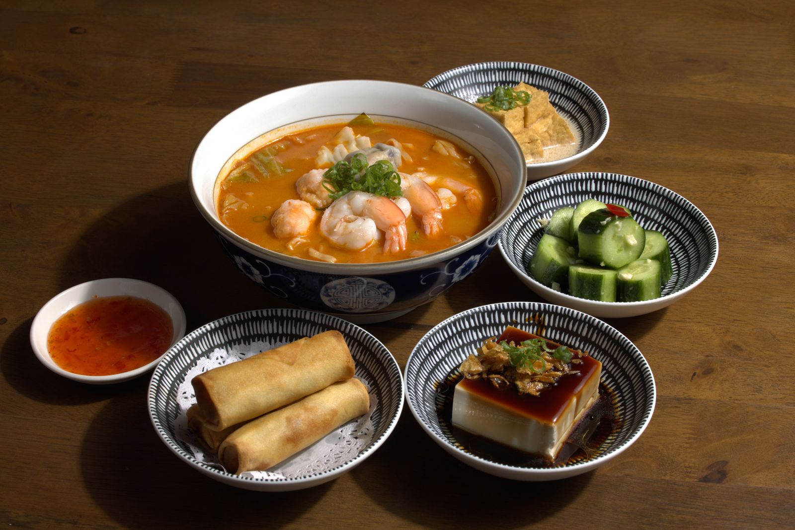 Laksa noodle bowl with prawns, spring rolls, chilled tofu, pickled cucumber, and braised tofu.